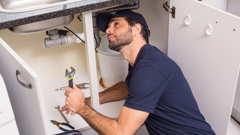 Plumber working on pipes under a sink